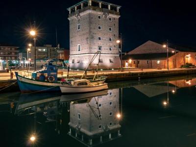 Torre illuminata di notte con riflessi sull'acqua e barche ormeggiate.