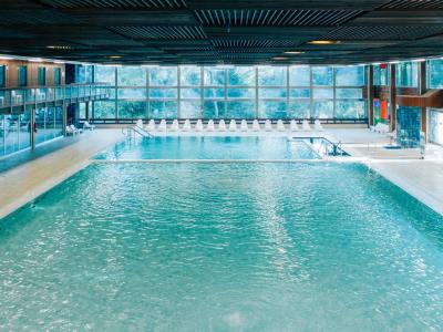 Piscina coperta con grandi finestre e sedie a sdraio bianche.