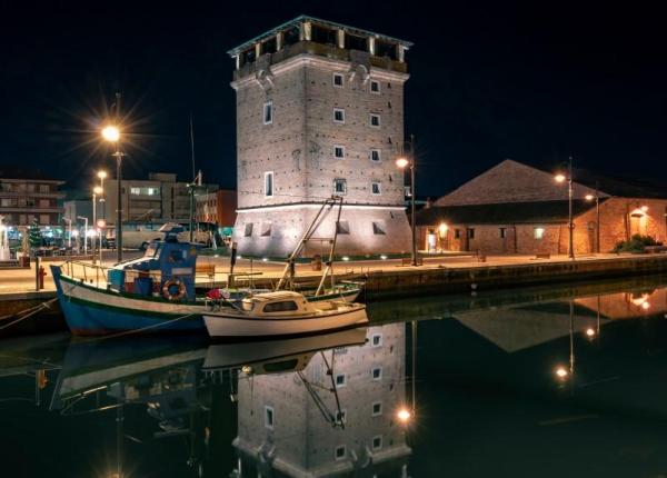 Historischer Turm bei Nacht beleuchtet, mit Booten, die sich im Wasser spiegeln.