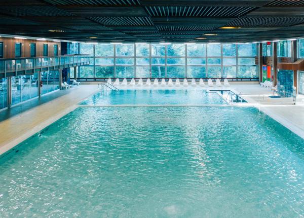 Piscina coperta con grandi finestre e sedie a sdraio bianche.