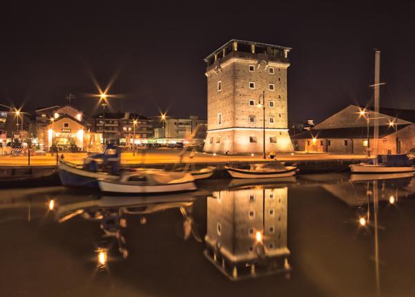 Torre storica illuminata di notte con riflessi sull'acqua.