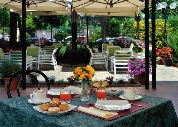 Colazione all'aperto con caffè, succo e dolci, circondata da fiori e verde.